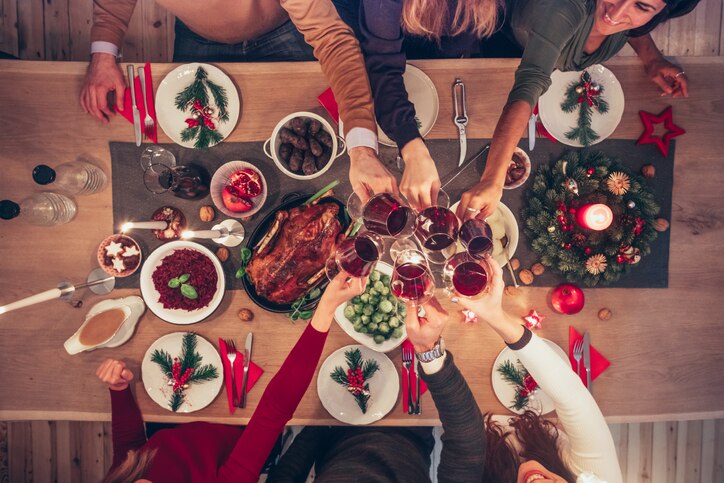 overhead view on people clinking wine glasses at christmas table with traditional german food