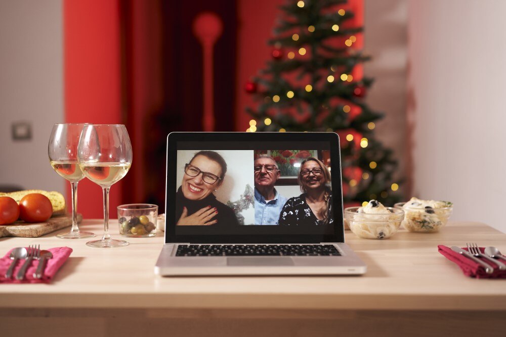 A festive Christmas dinner setting with a laptop on the table displaying a video call with a smiling family
