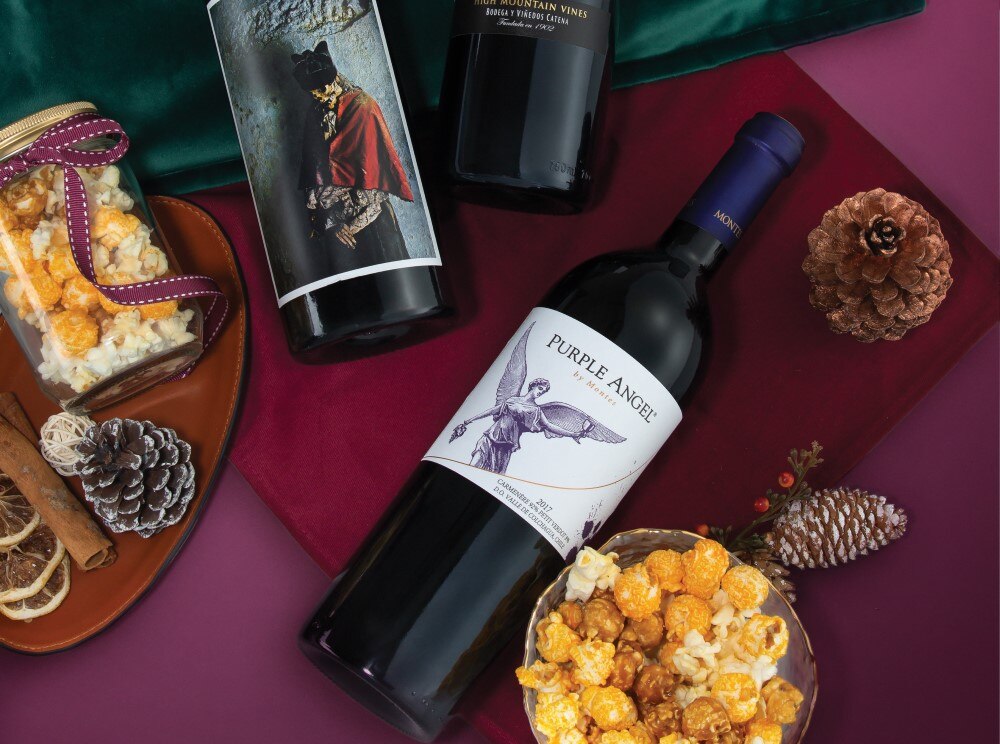 A stylish composition featuring a bottle of Purple Angel red wine, gourmet popcorn, and other luxurious bottles of wines