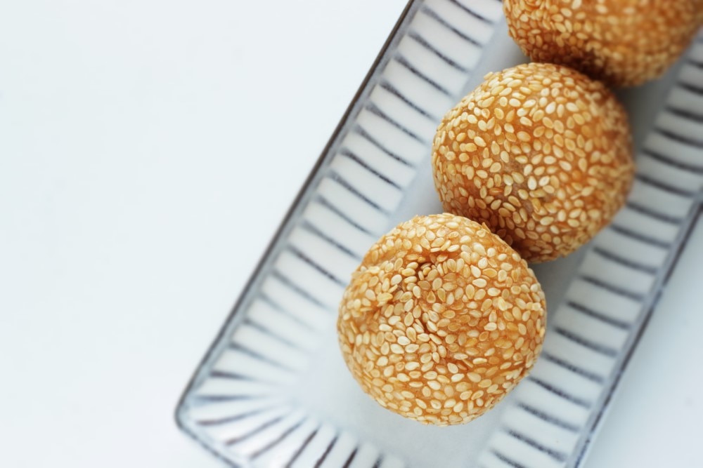 Golden sesame seed balls neatly arranged on a striped ceramic plate with a minimalist white background for Chinese New Year