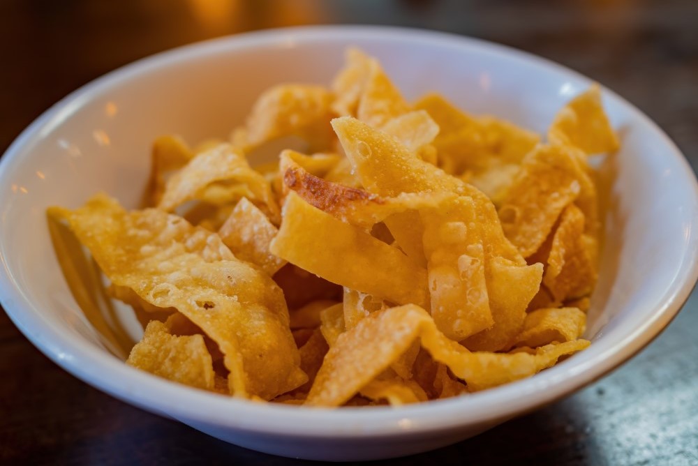 A bowl of crispy golden-brown wonton chips on a wooden table for celebrating Chinese New Year